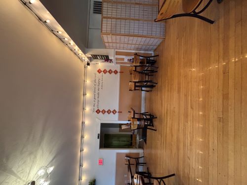Fairy lights decorate the top of an open room. Small tables are spaced apart on a wooden floor.