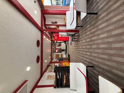 Deli bench seating flank the camera. Further down the hall are drink machines and the order counter