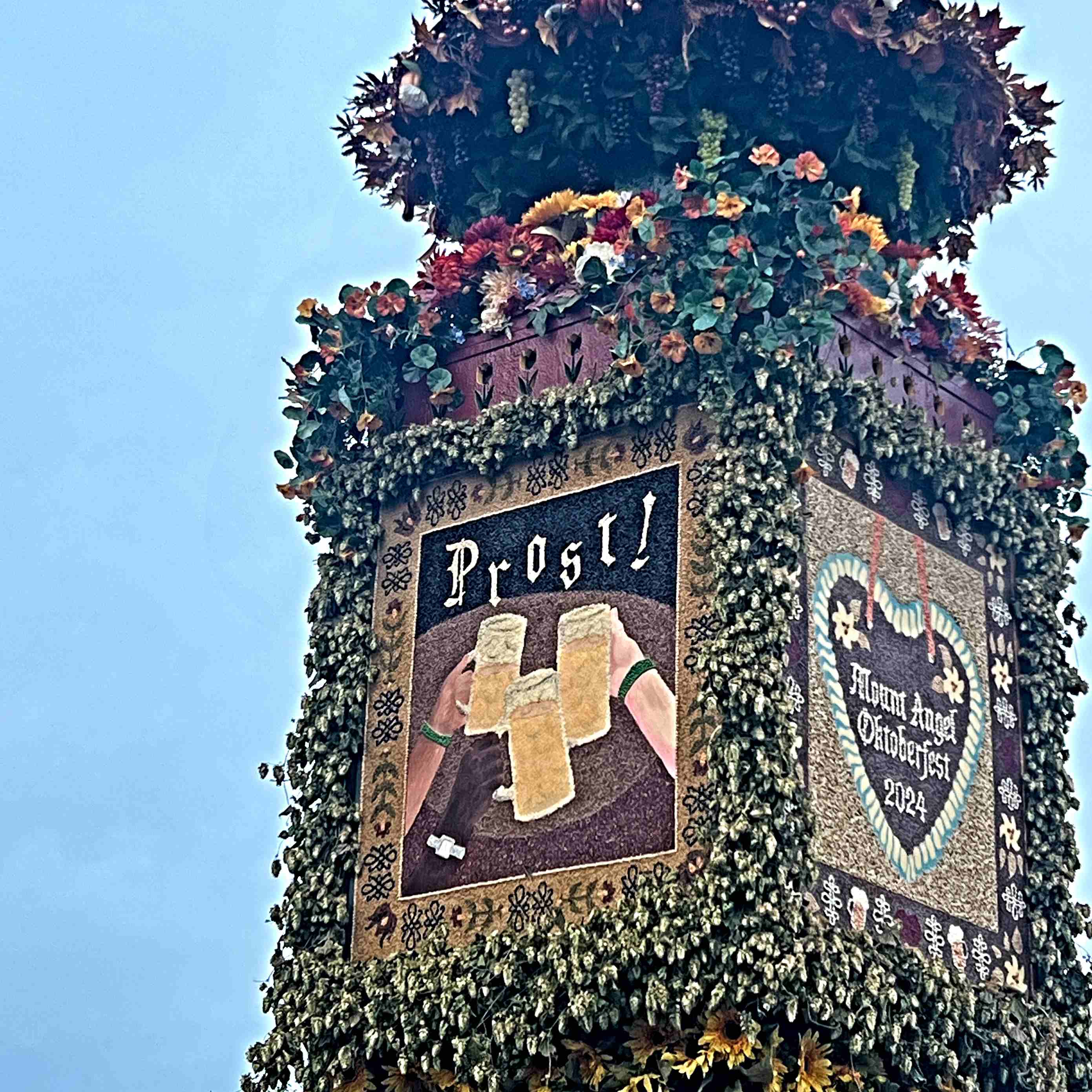 A flower covered post with art for Mount Angel and Prost