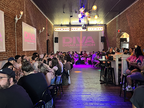 a group of people at tables await an event with a disco ball and fun lighting.