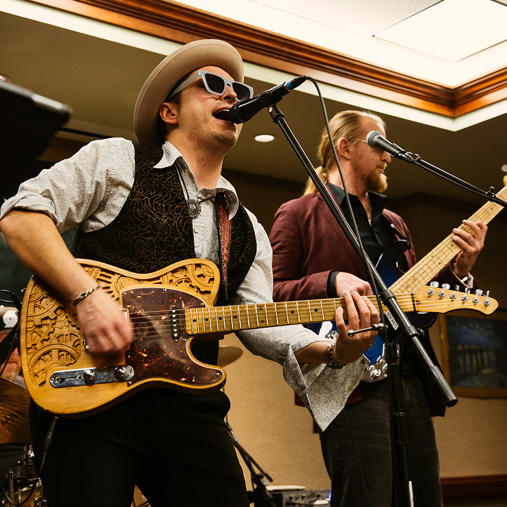 two male musicians on stage singing into microphones while playing guitar