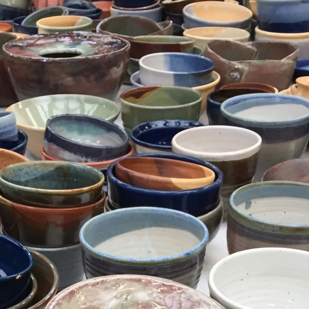 Assortment of handmade ceramic bowls and cups in varied shapes, sizes and earthy glazes, including blue, green, brown, cream and rust.