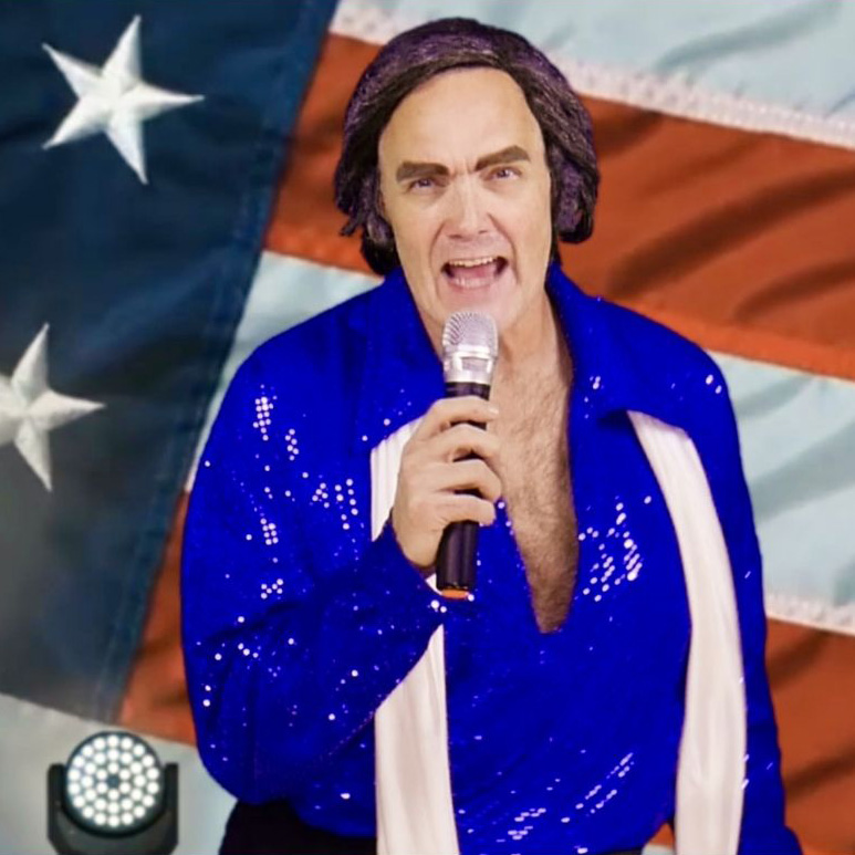 Man in a sparkly blue shirt singing into a microphone in front of an American flag backdrop.