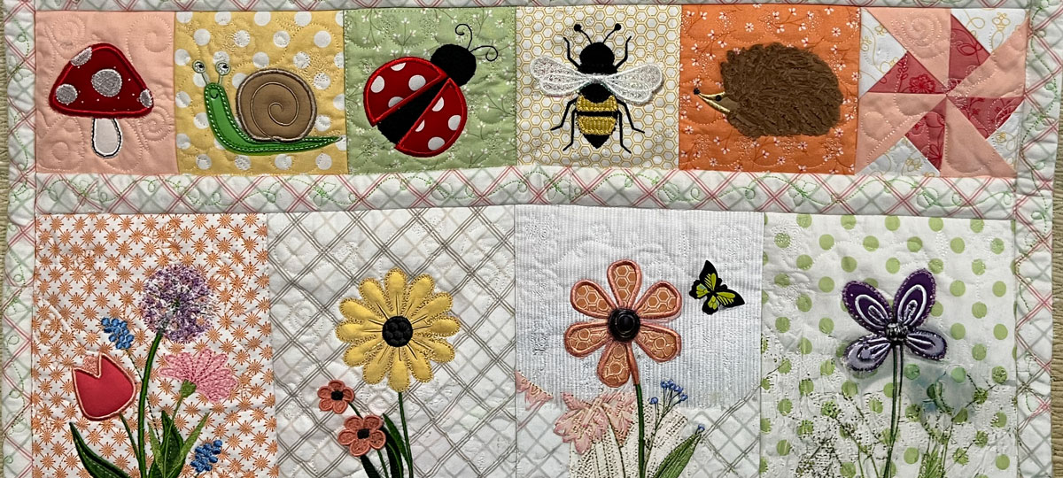Colorful handmade quilt featuring embroidered flowers, butterflies, mushrooms, a snail, ladybug, bee, and hedgehog. Pastel fabrics, decorative stitching, and patchwork blocks create a whimsical garden scene.