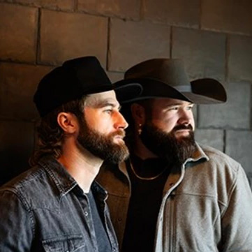 two bearded men in denim shirts and cowboy hats looking off into the distance