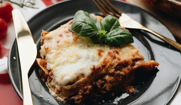 plate of a larger piece of lasagna with sprig of basil on top of crusty cheese
