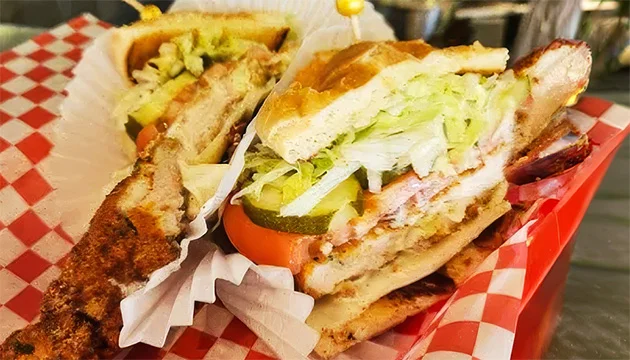 Grilled sandwich from DK's Grill cut in half and served in a red basket with lettuce, tomato, pickles and melted cheese on toasted bread.