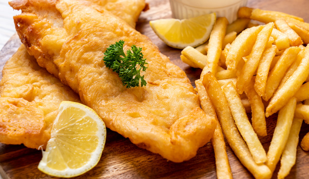 Fisherman's Seafood Market fish and chips with golden fried fish fillets, French fries, lemon wedges and parsley, served on a wooden board.
