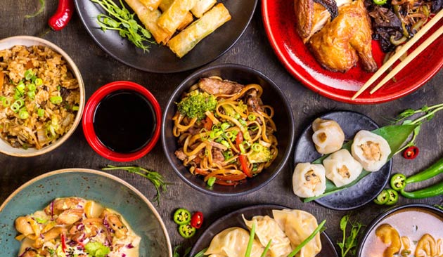 Lucky Dragon Grill assortment of Asian dishes including noodles, fried rice, dumplings, spring rolls, shrimp dumplings and roasted chicken, served in colorful bowls and plates.