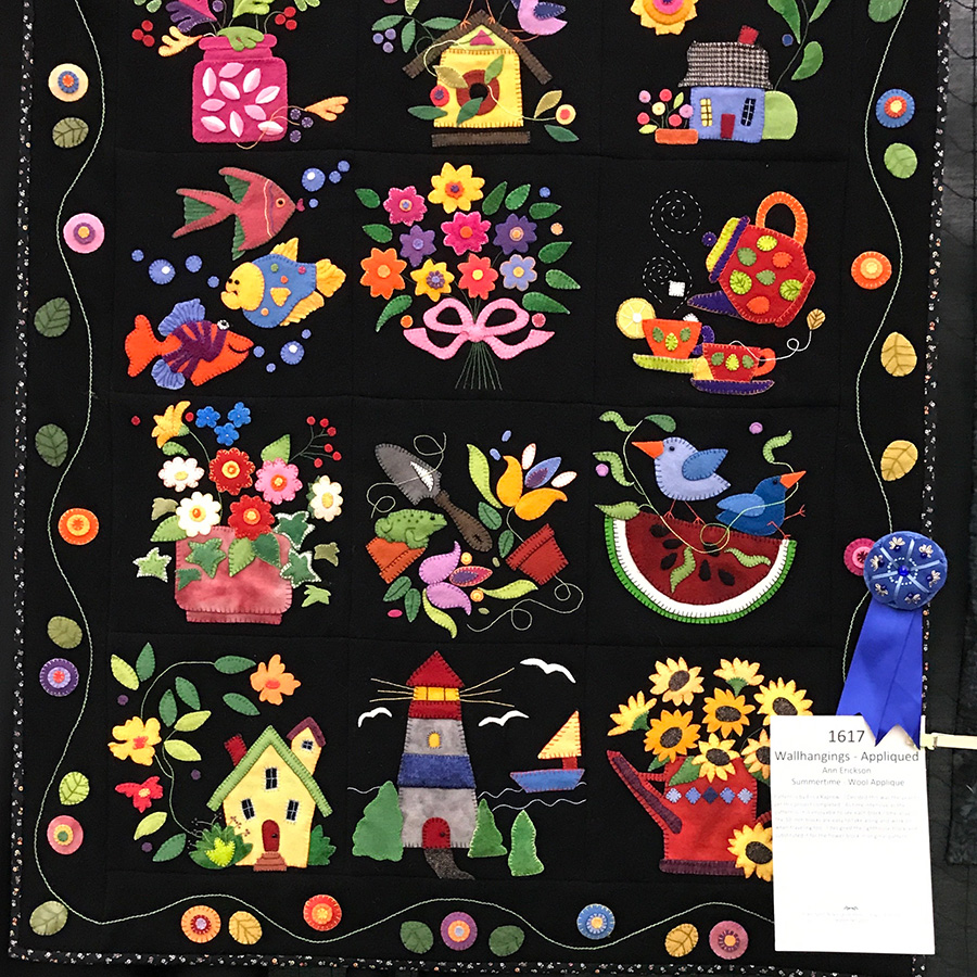 Colorful appliqué quilt featuring whimsical summer-themed panels, with a blue ribbon award attached.
