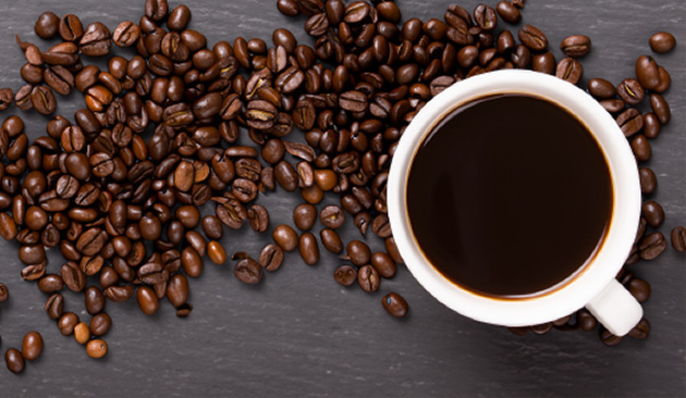 Espresso Mill and Bakery cup of freshly brewed black coffee surrounded by roasted coffee beans on a dark surface, highlighting the bakery's coffee offerings.