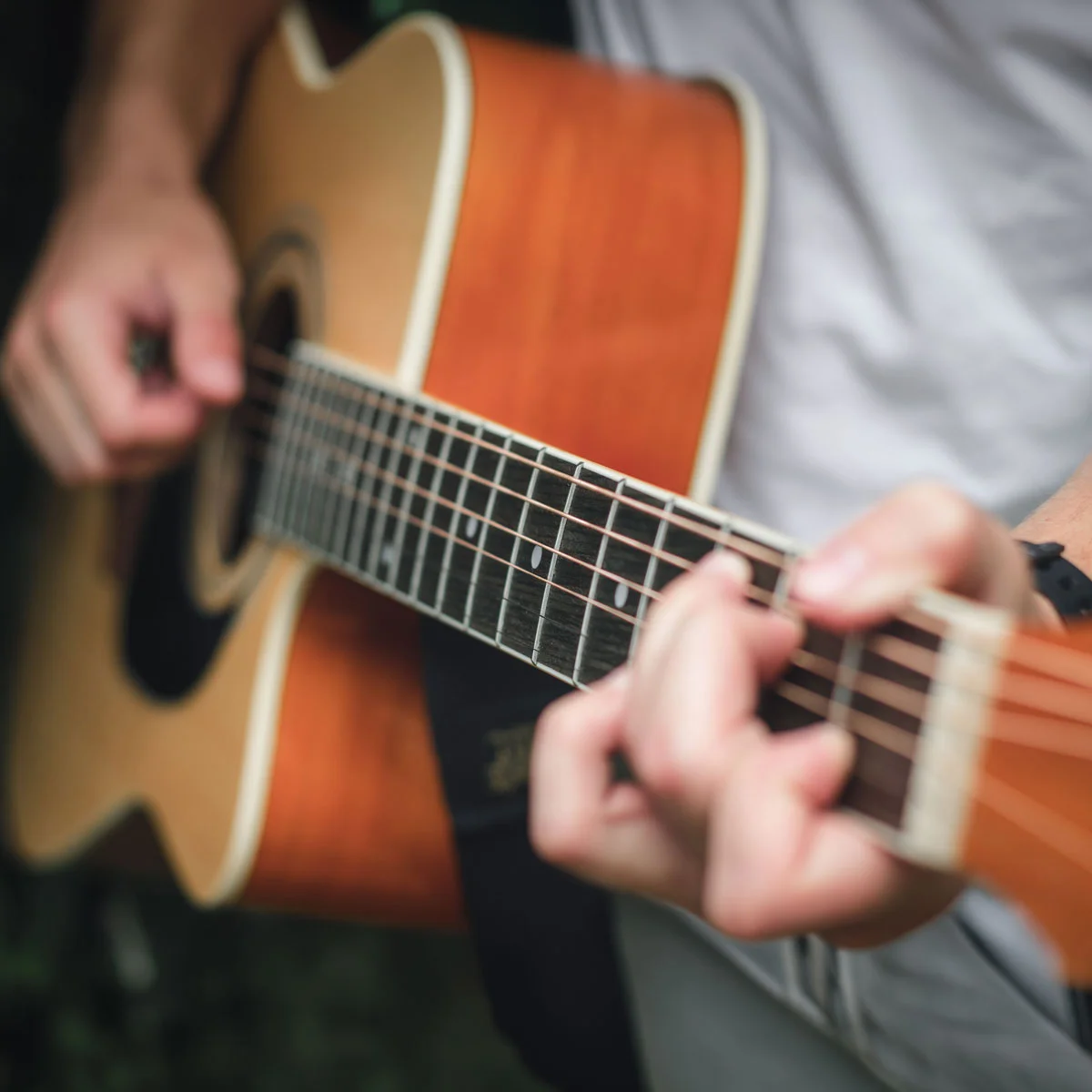 A close-up view of hands playing an acoustic guitar, with the strings and fretboard in sharp focus while the musician and background are softly blurred.