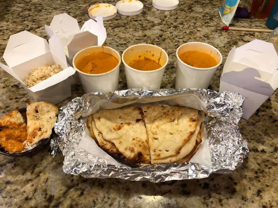 American Market displays Indian takeout including naan bread, rice and three curry dishes arranged on a kitchen counter with containers ready for sharing.