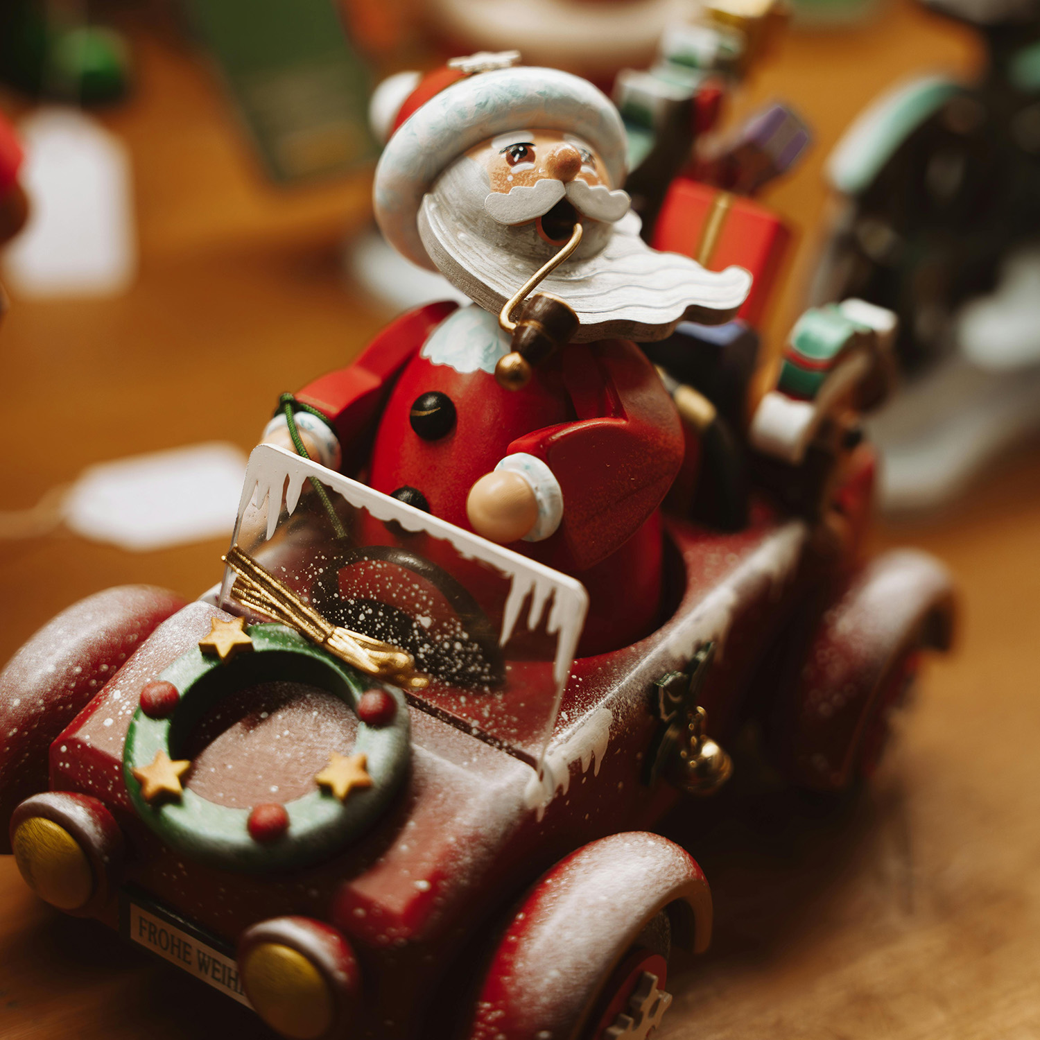 Close-up of a festive Santa Claus figurine driving a red holiday car decorated with a wreath and presents.