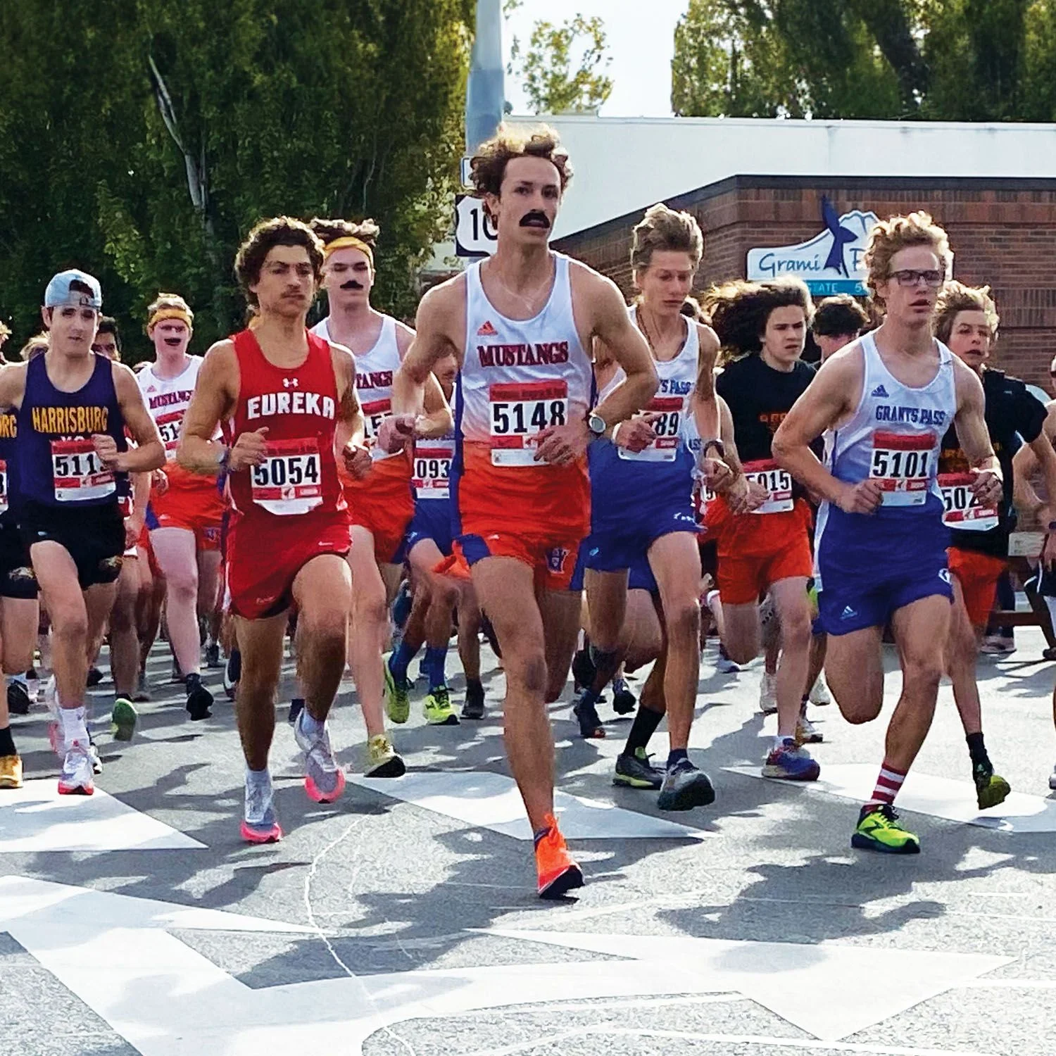 Runners sprint from the starting line during the Prefontaine Memorial Run in downtown Coos Bay, with competitors in colorful race uniforms filling the street.