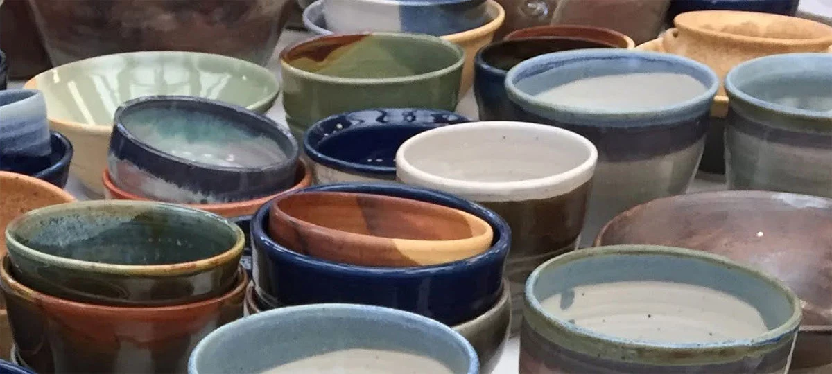 Assortment of handmade ceramic bowls and cups in varied shapes, sizes and earthy glazes, including blue, green, brown, cream and rust.