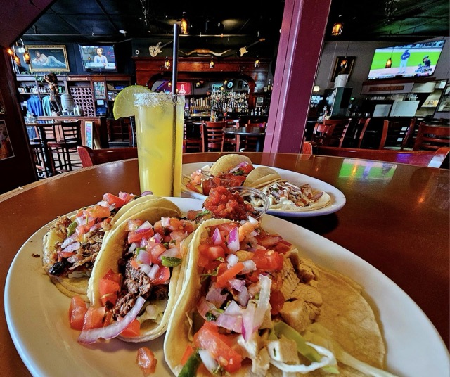 two plates of tacos and a Margarita placed on a high top table in a pub