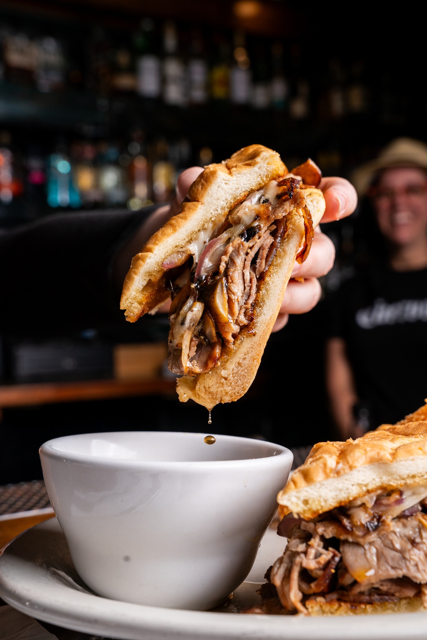 hand holds half of a French dip sandwich over ramekin of jus