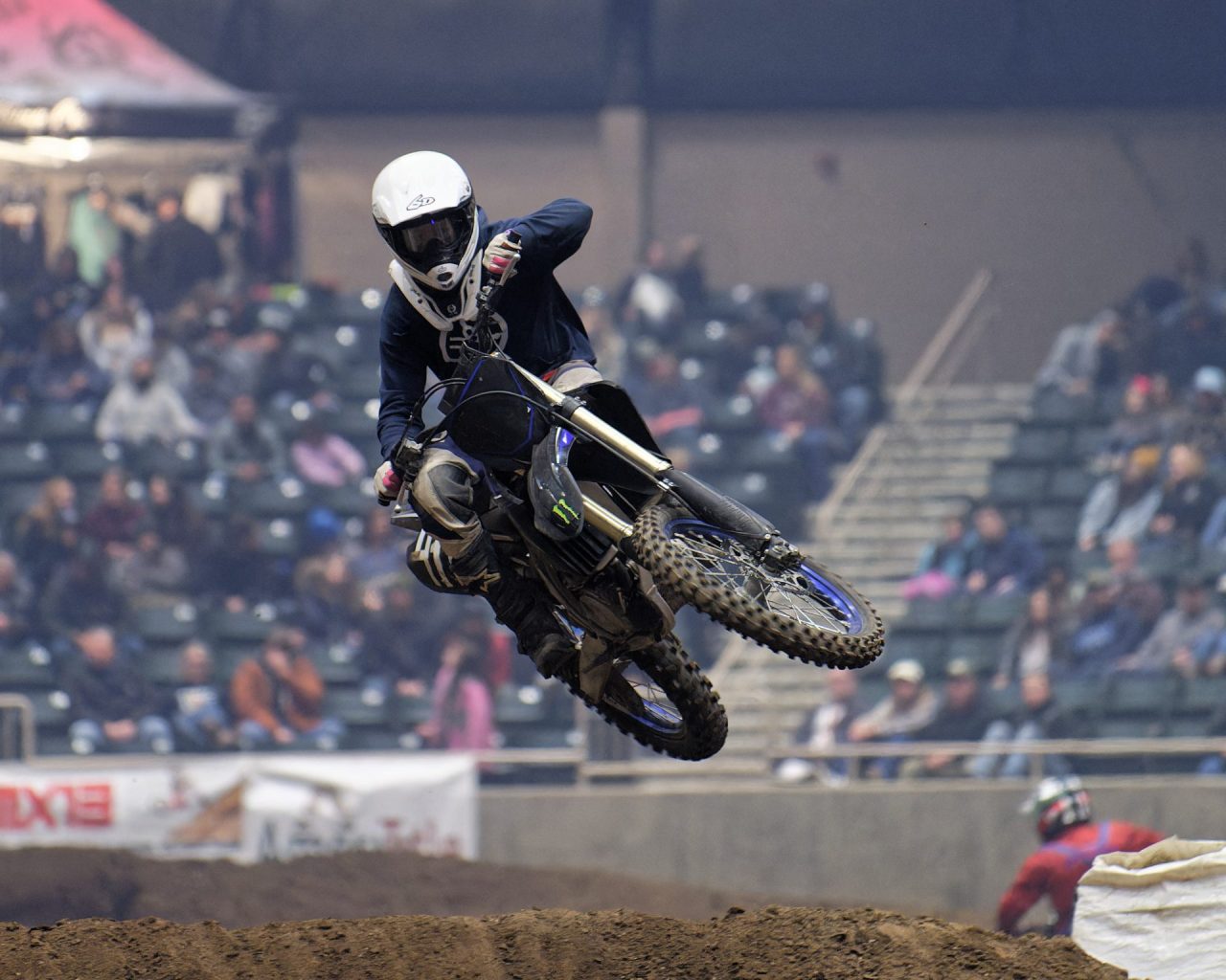 Person riding motorbike going over a dirt jump in an arena