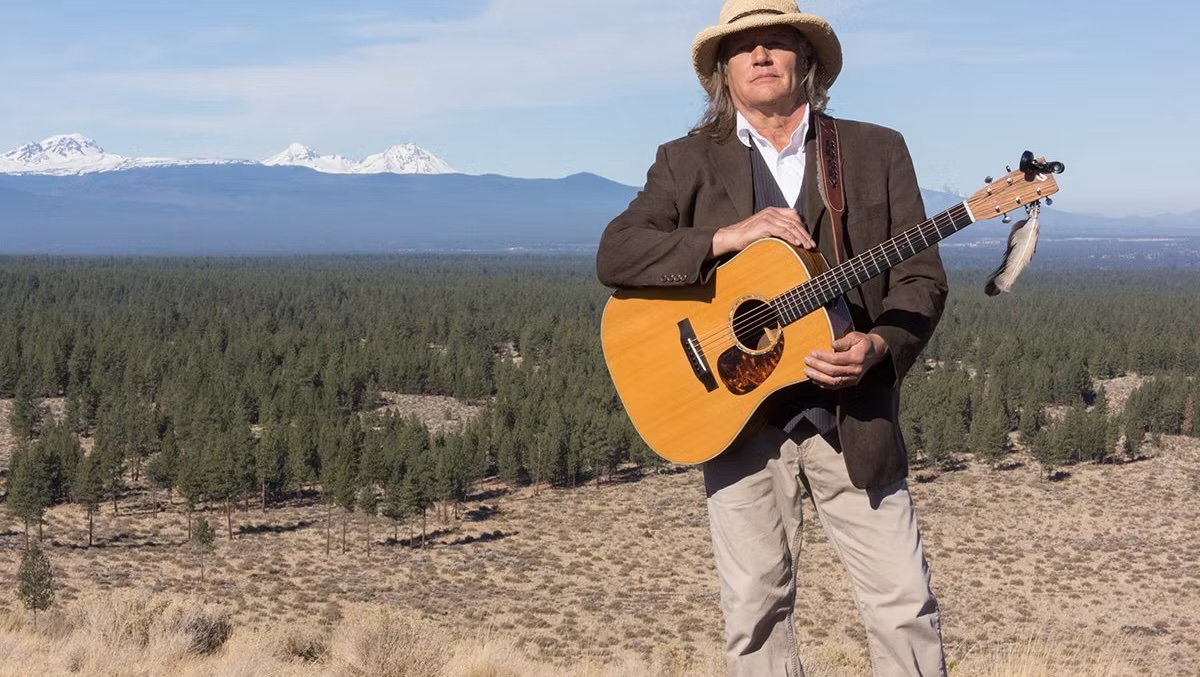 Bobby Lindstrom holding guitar in front of mountains