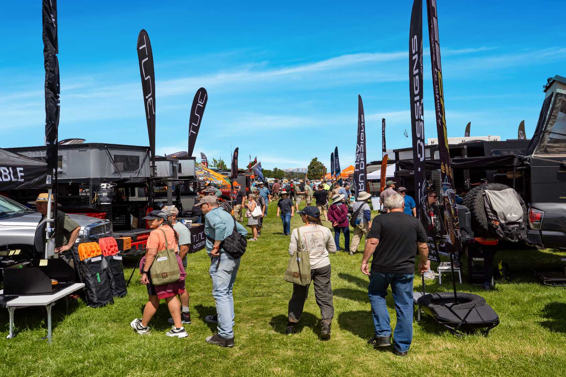 People walking around busy field filled with overlanding rigs.