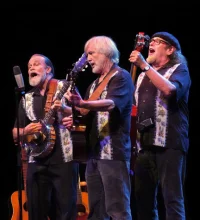 three men on a stage playing banjos and a guitar