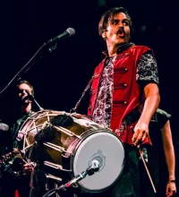 A man in a red vest with a drum in front of him