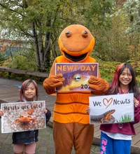 Two kids posing with a person dressed in a newt suite holding signs