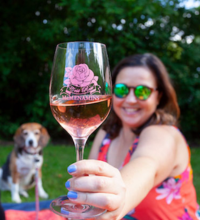 Woman holding up a glass of rose wine with a flower on it. A dog sits in the background