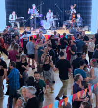 Crowd of people dancing in a large room with a band in the background