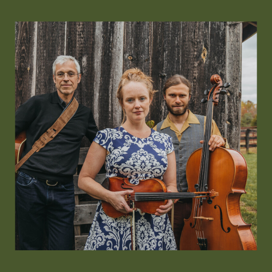Three people with stringed instruments in front of an old barn