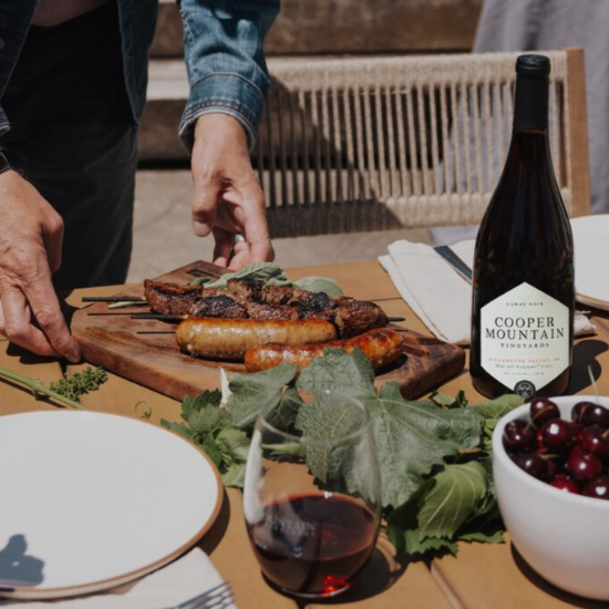 Someone placing a wooden board down with skewered meets, next to a glass and bottle of wine