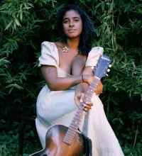 Leyla McCalla with a guitar against a plant background