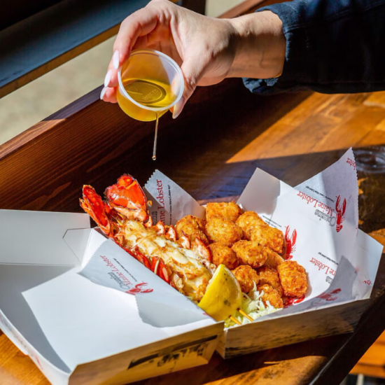 Butter sauce being poured onto a lobster with tater tots and a lemon next to it