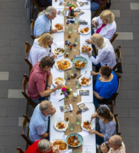 An aerial view of people gathered along a table, eating a meal
