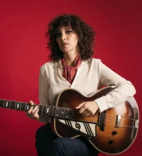Gaby Moreno holding a guitar against a red background