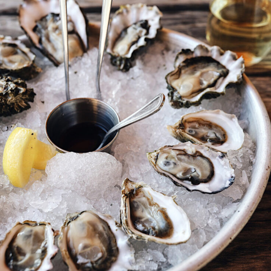 Tray of ice with oysters, lemon, and a cup of sauce