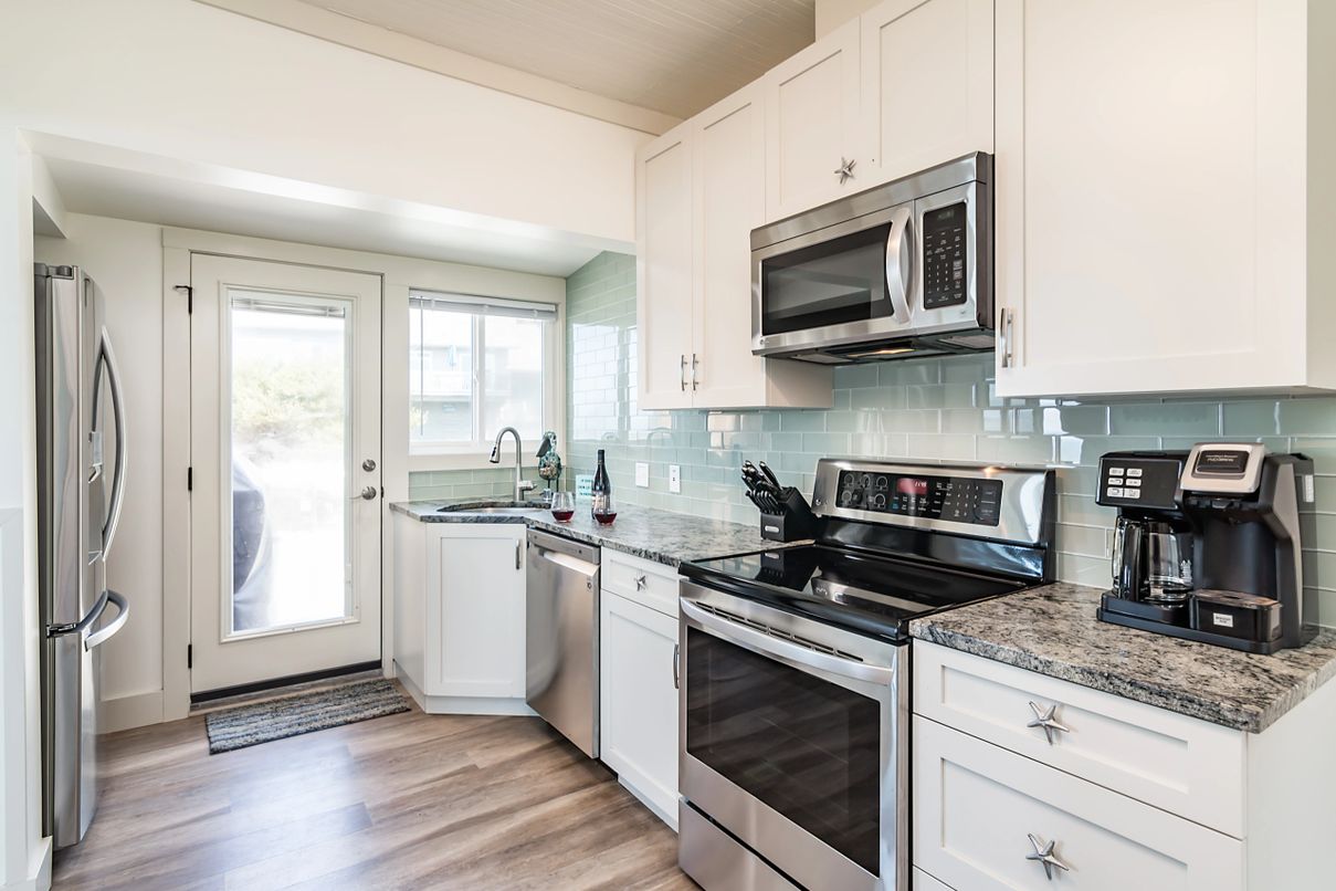 White kitchen with seafoam tile and stainless-steel appliances with glass door to the outside.