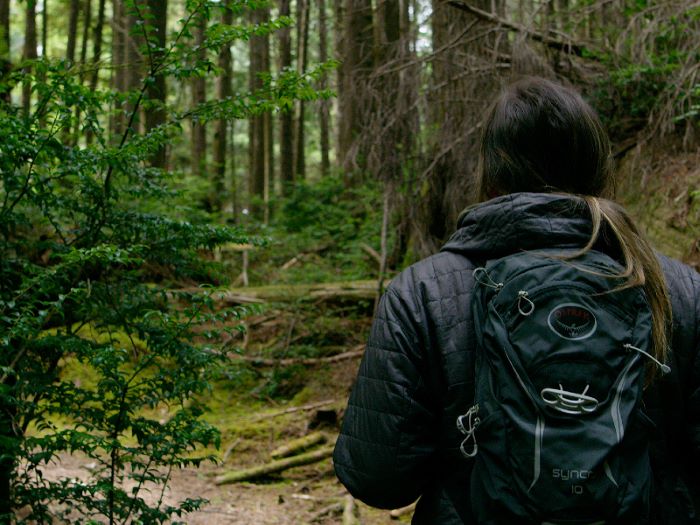 View from the back of a hiker carrying a backpack while walking on a forested trail.