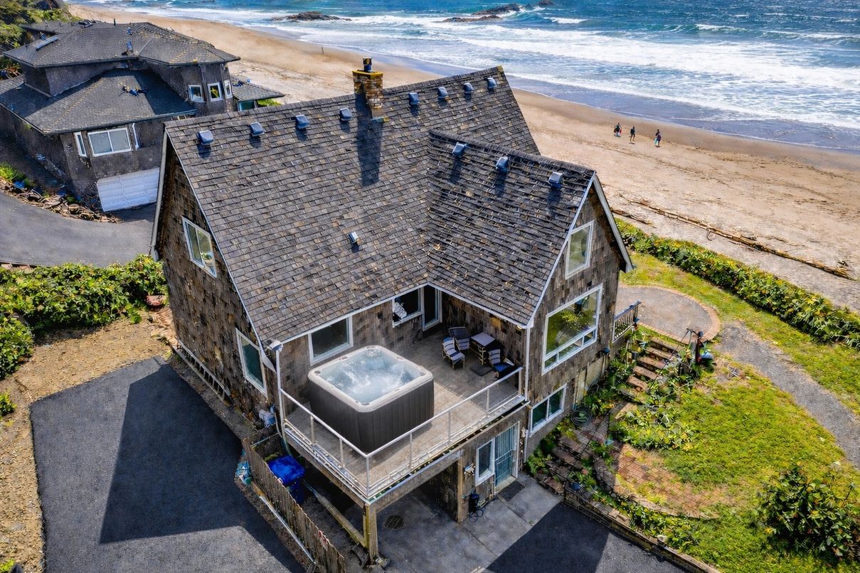 Overhead view of Cape Cod style two-story house on the beach with deck hot tub and grassy area.