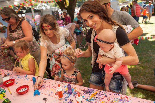 Two women and three children interact at an art vendor booth.