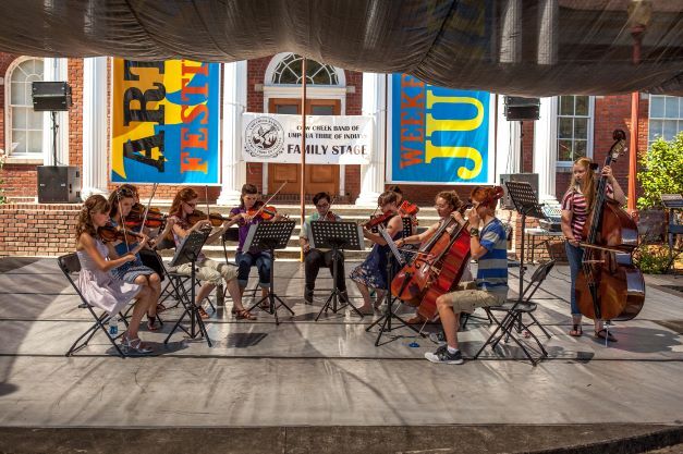 A youth ensemble performs on stage with stringed instuments.