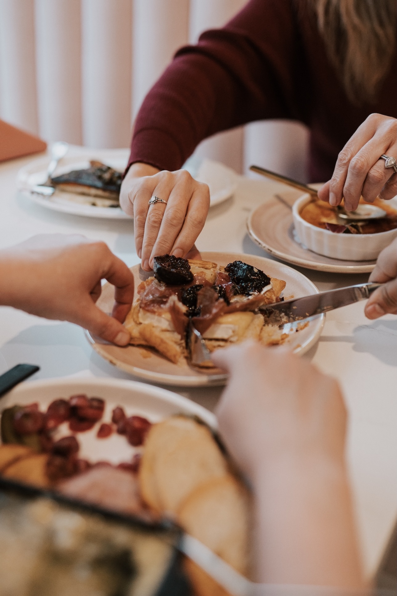peoples hands reaching for shared appetizer on a table with multiple plates of food
