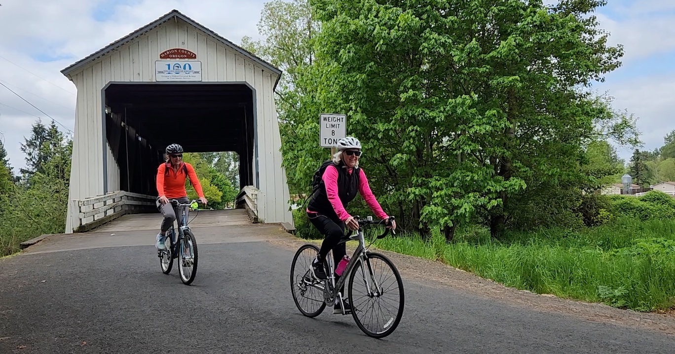two bicyclists riding away from a covered bridge