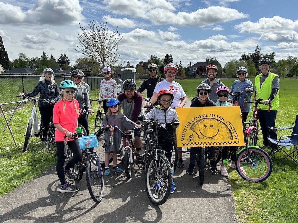 a group of children and adults gathered behind a yellow sign reading "Monster Cookie Metric Century"
