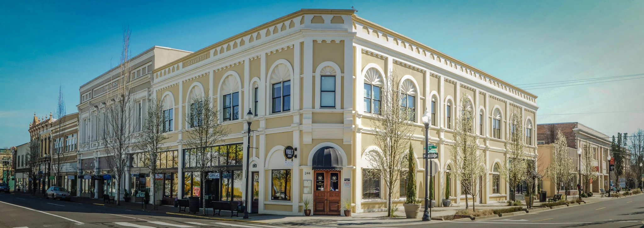 Wide shot of large beige historic building with trees and lampposts lining the sidewalks.