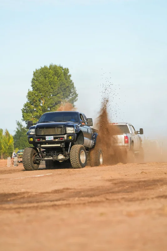 Two large monster trucks kicking up dirt in a game of tug o war