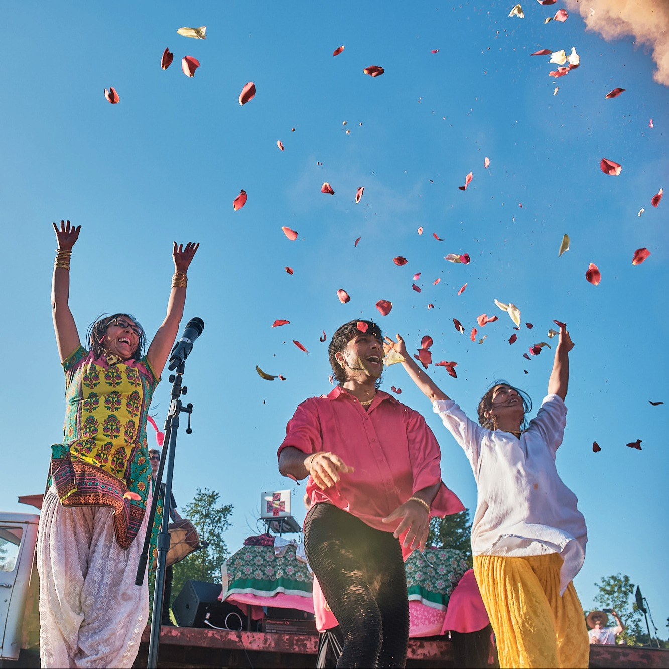 Three people on a stage at a Holi festival.