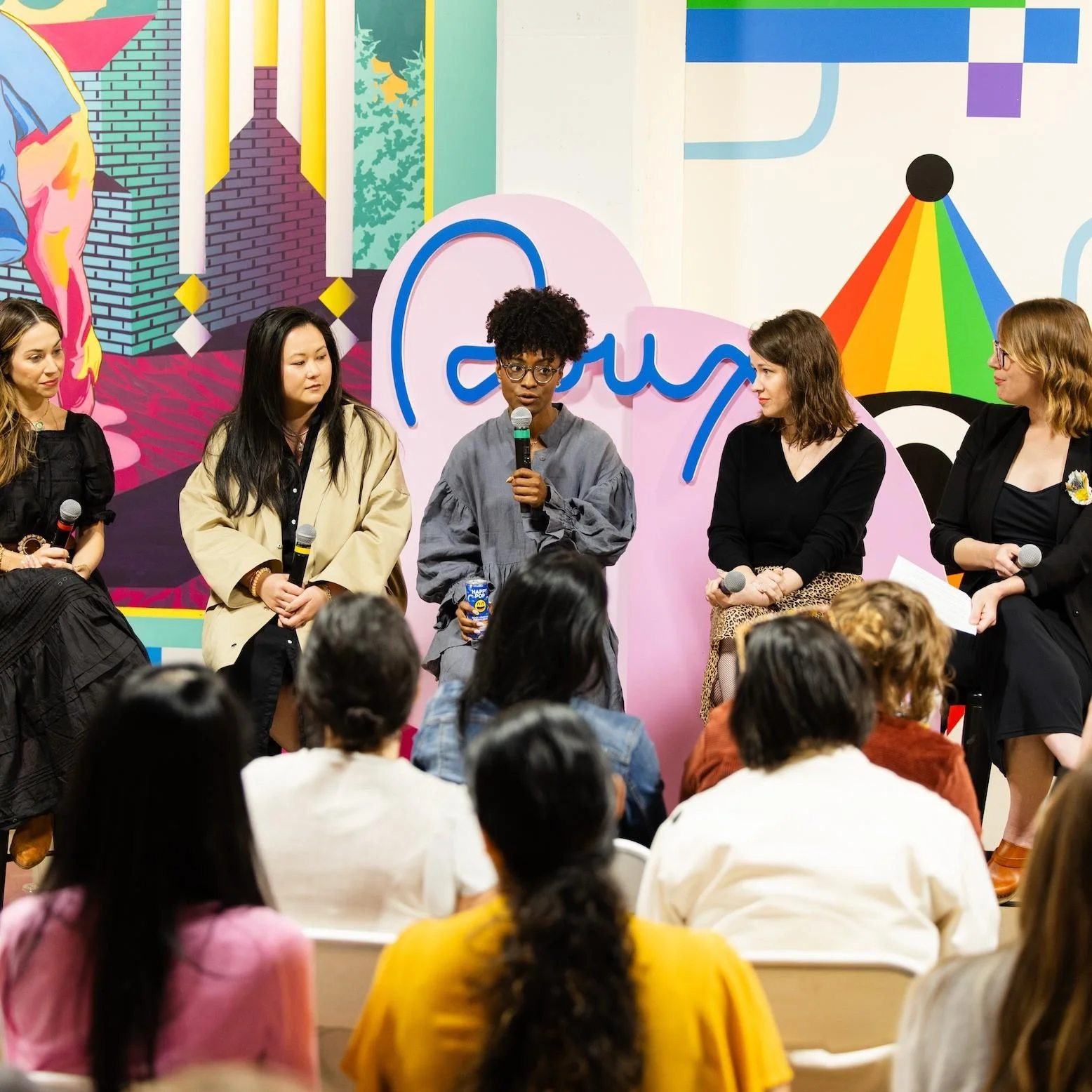 Panel of women seated on a stage in front of a colorful background.