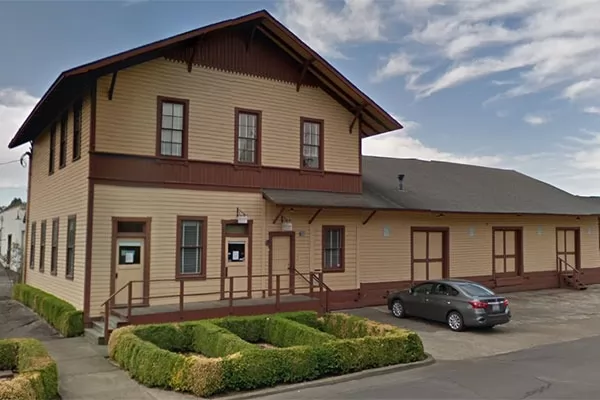 Tan and red building with grey car parked in front.